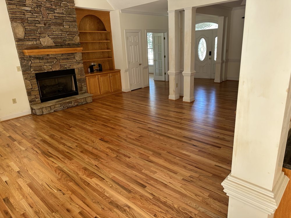 Refinished red oak hardwood floors flowing through an open concept living room with stone fireplace